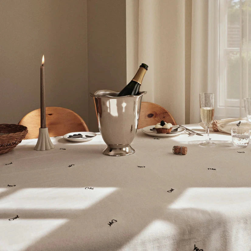 Silvrig vinkylare med champagneflaska i på ett dukat bord med vit uk med tulpaner på. Levande ljus och glas, furustolar.