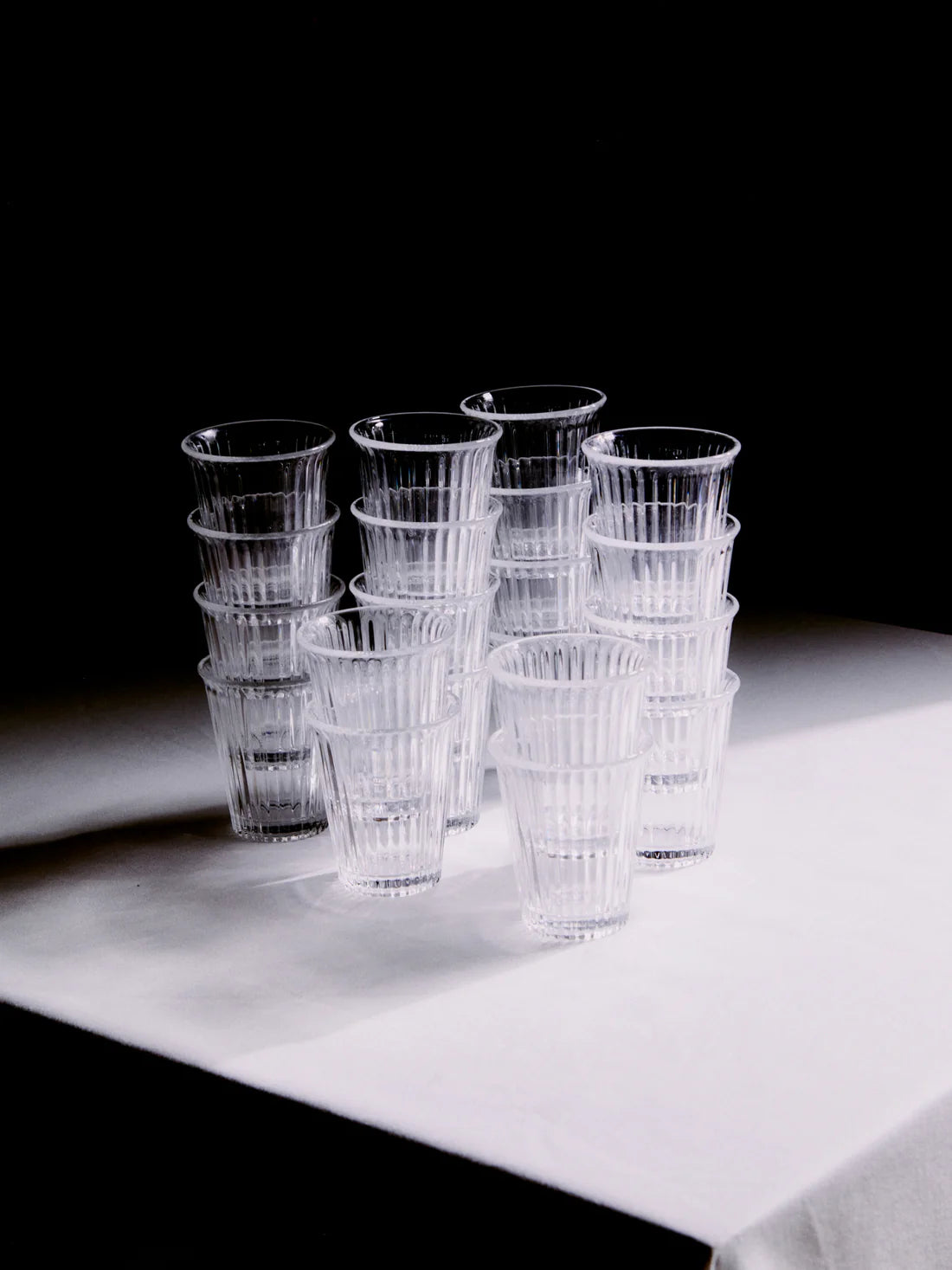 Massa glas från Service Projects staplade på ett bord med vit duk och svart bakgrund