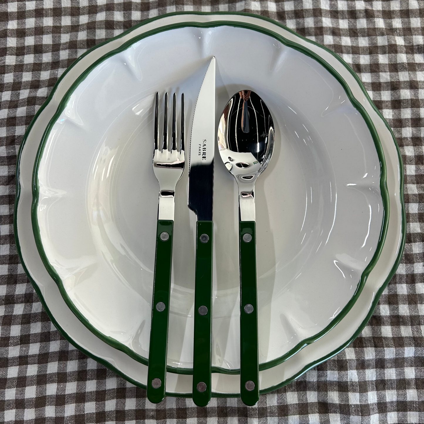 Dukning på brunrutig duk med porslin med grön kant och mörkgröna bistrobestick från Sabre Paris. Fotat på Mon Bistro & Friends