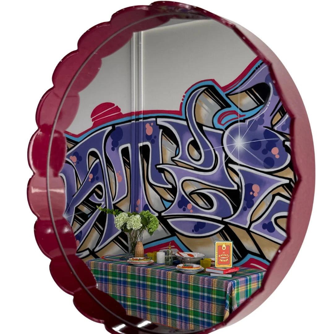 Vinröd rund vågig spegel med grafitti och dukat bord som speglas i spegeln.