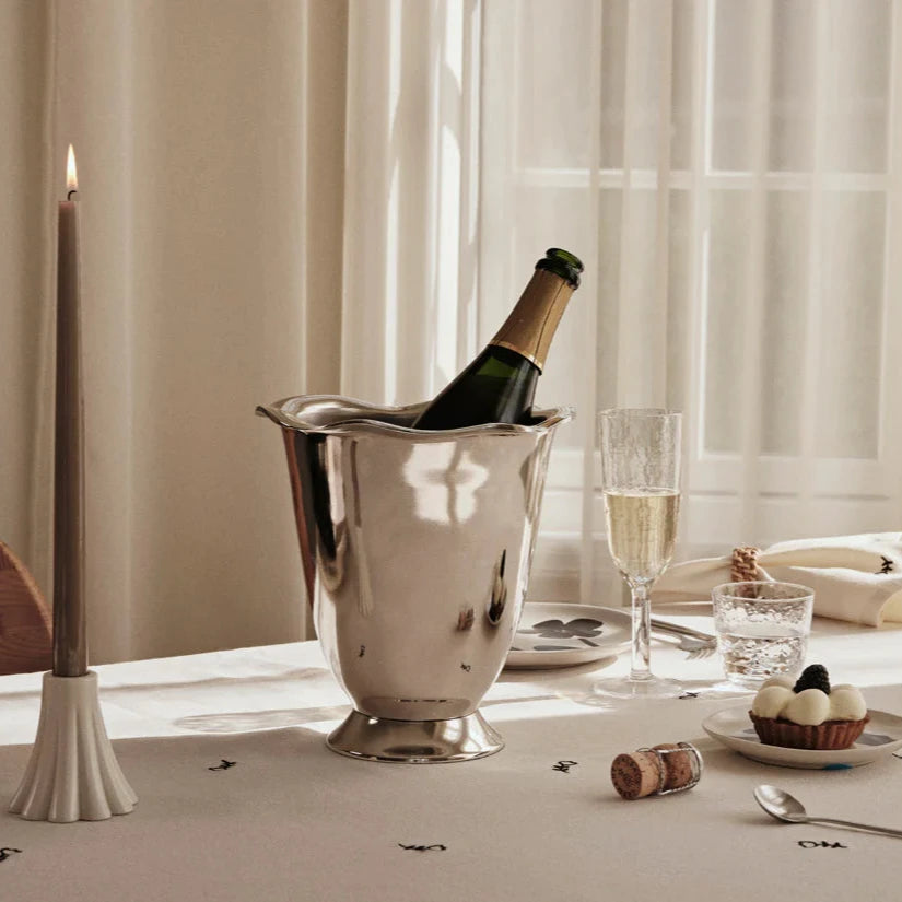 Silvrig med champagneflaska i på ett dukat bord med levande ljus och glas.
