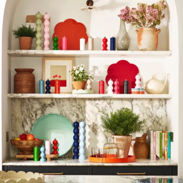 MÄnga pepparkvarnar i olika fÀrger i en marmorbokhylla