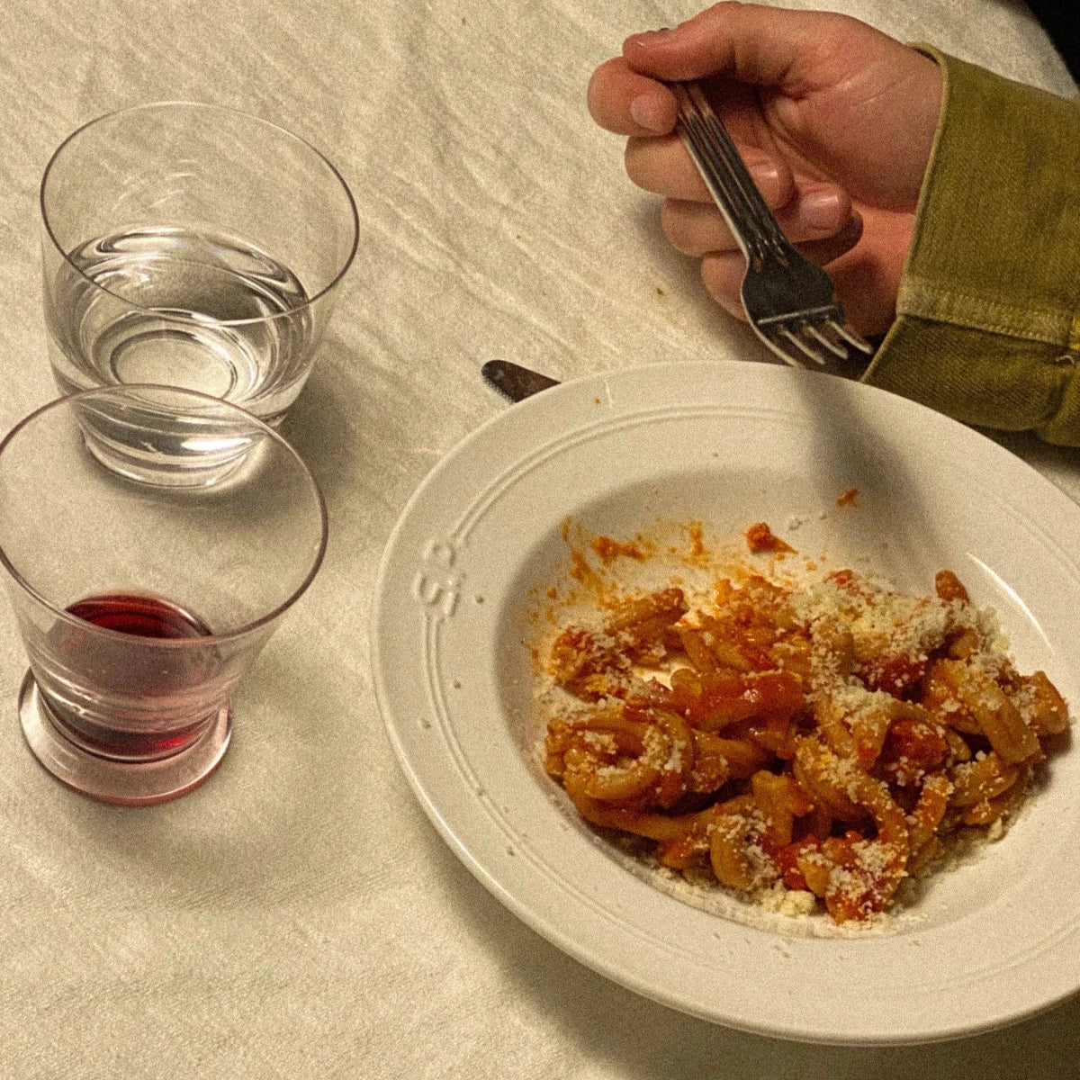 Djup tallrik från Service projects fylld med pasta, en person äter ur tallriken, den står på ett bord med vit duk och ett vin och ett vattenglas