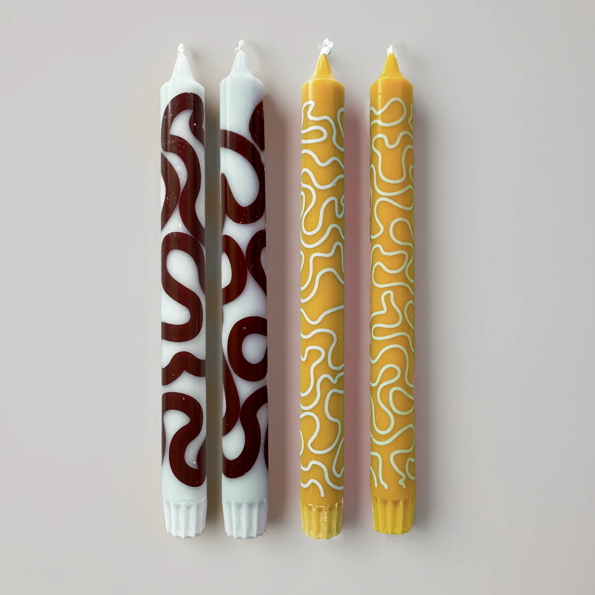 Fyra stycken stearinljus i brunt, gult och mintgrönt med mönster mot vit bakgrund