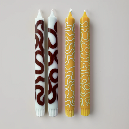 Fyra stycken stearinljus i brunt, gult och mintgrönt med mönster mot vit bakgrund