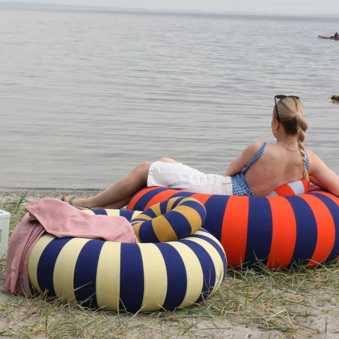 Studio about sittpuffar I glada färger på en strand, en kvinna sitter i en
