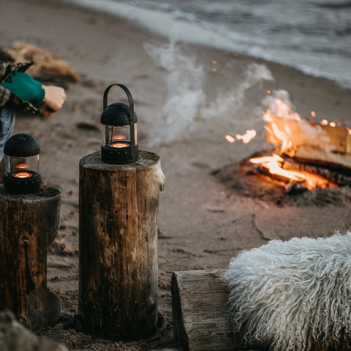 Transparent light speaker utomhus vid öppen eld på en strand ståendes på trästubbar