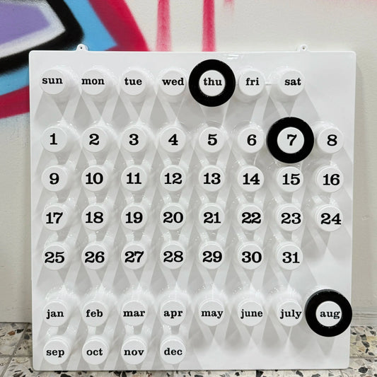 Vit väggkalender med svarta ringar ståendes på golvet lutad moet graffitivägg