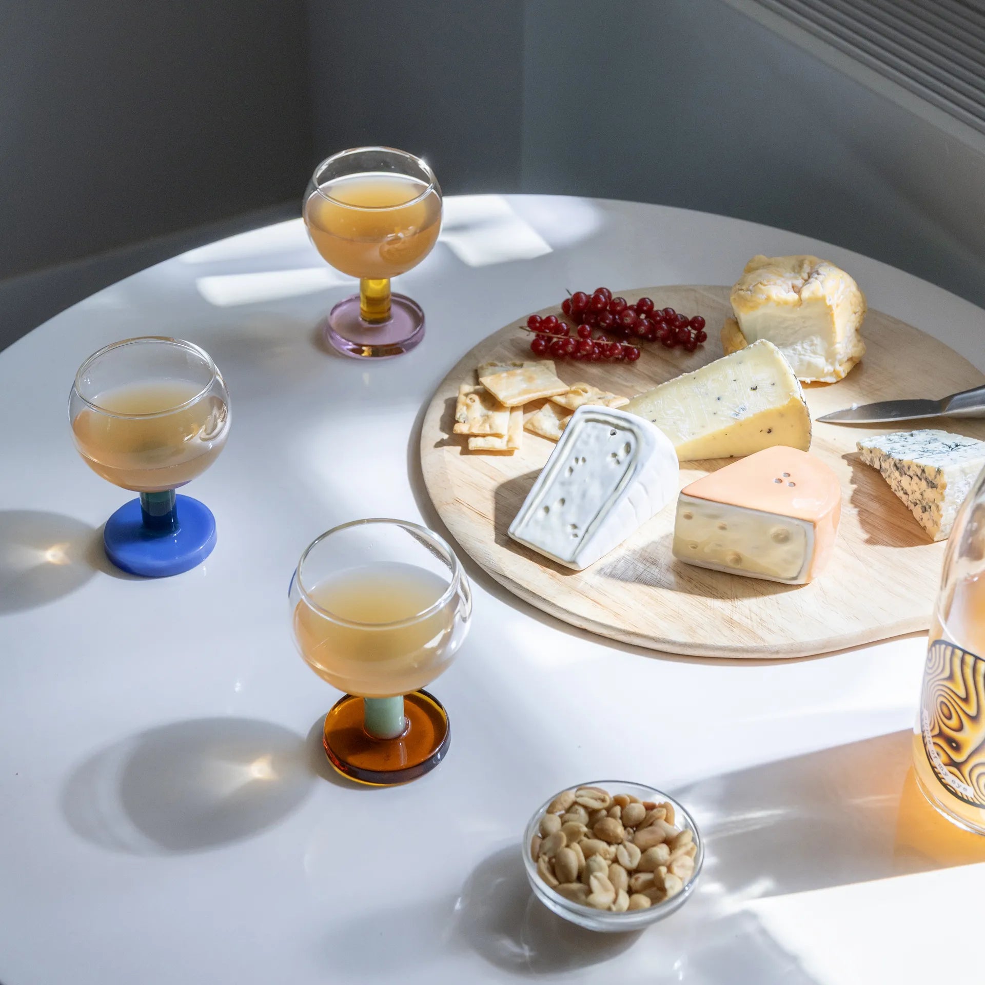 Dukat bord med vinglas i olika färger från & Klevering med orangevin i och med en ostbricka på bordet.