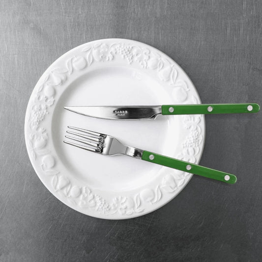 sabre bestick kniv och gaffel mörkgrön på vit tallrik på rostfri bordsyta bild tagen uppifrån