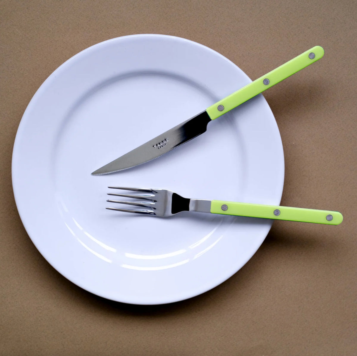 sabre bistrot kniv gaffel på vit tallrik mot brun bakgrund