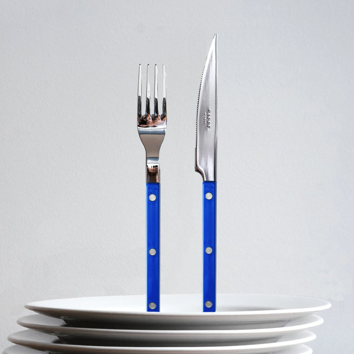 sabre bistrot kniv gaffel ståendes på hög med vita tallrikar
