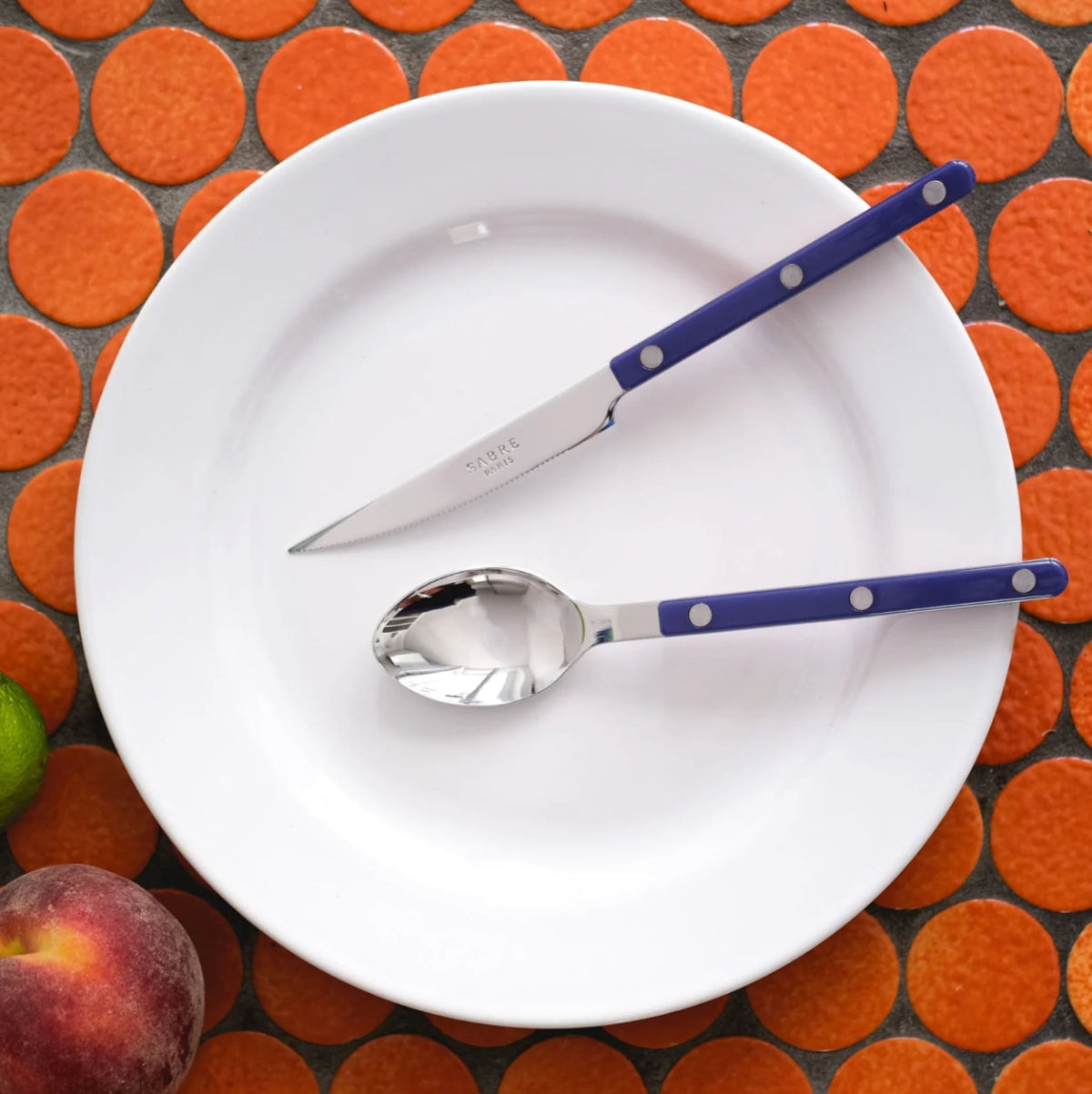sabre bistrot kniv gaffel marinblå på vit tallrik mot orangeprickig bakgrund