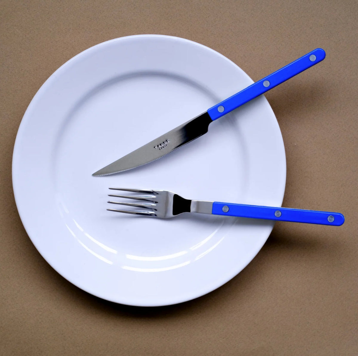sabre bistrot blå kniv gaffel på vit tallrik mot brun bakgrund