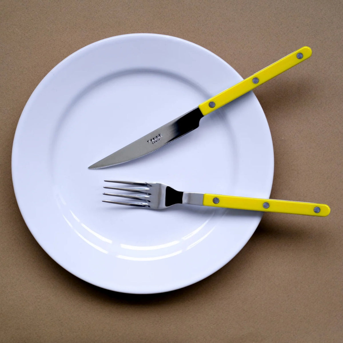sabre bistrot kniv gaffel på vit tallrik mot brun bakgrund