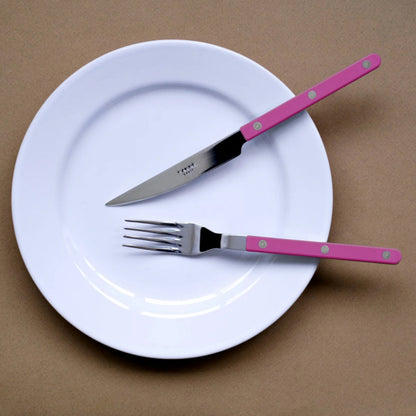 sabre bistrot kniv gaffel på vit tallrik mot brun bakgrund