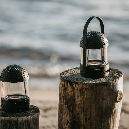 Transparent light speaker svart två stycken på två trästubbar utomhus, vattenbryn i bakgrunden